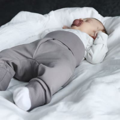 Vauva makaa tutti suussa harmaat housut jalassa. 