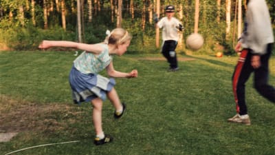 Lina som barn när hon spelar fotboll med sina bröder på en sommaräng. Hon har precis sparkat iväg fotbollen.