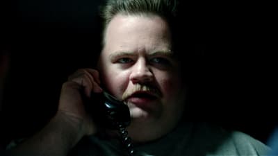 Närbild på Richard Jewell (Paul Walter Hauser) då han sitter i ett mörkt rum och håller i en telefonlur.