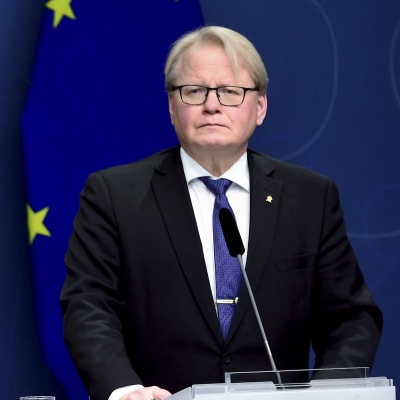 Sveriges försvarsminister Peter Hultqvist står vid ett talarpodium framför Sveriges och EU:s flaggor.