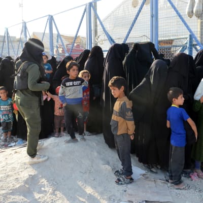En person vaktar människor i ett läger i Syrien.