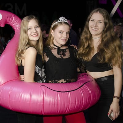 Tre tjejer. Två av dem poserar med en rosa uppblåst flamingo. 