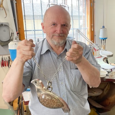 Kultaseppämestari Juha Janger pitelee käsissään hopeasta ja kivestä tehtyä isoa riekkoriipusta.