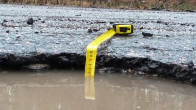 En vattenfylld grop i asfalten med ett måttband nerstucket. Måttbandet visar på lite under sju centiometer vatten.