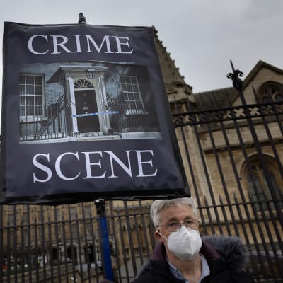 En demonstrant håller upp ett plakat med texten "Crime Scene". Han står utanför Downing Street 10