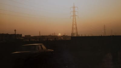 Valokuvassa näkyy auringonlasku ja voimalinjoja kaupungin edustalla