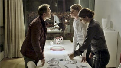 Scen ur serien mammon där Peter, Andreas och Eva står runt ett bord
