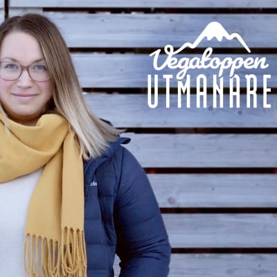 en kvinna i gul halsduk och öppen jacka står utomhus framför en stor trägrind