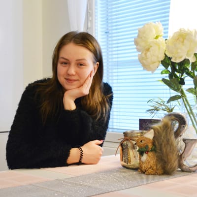 En ung kvinna sitter vid ett köksbord och lutar kinden mot den ena handen.