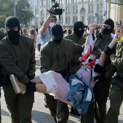 Män från säkerhetsstyrkorna, iklädda svarta huvor, bär bort en kvinnlig demonstrant under en demonstration i Minsk den 26 september 2020.