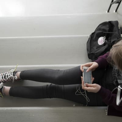 Nuori nainen katsoo kännykkää rappukäytävässä.