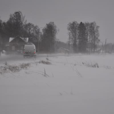 Bil på väg längs landsväg i snöyra och hård vind.