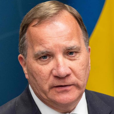 Stefan Löfven, en vit man, i kostym med Sveriges flagga i bakgrunden.