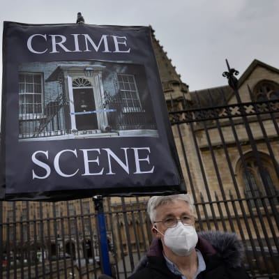 En demonstrant håller upp ett plakat med texten "Crime Scene". Han står utanför Downing Street 10