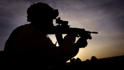 Konturerna av en beväpnad, hjälmbeklädd soldat i solnedgång i Afghanistan.