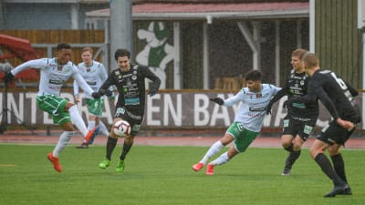 EN spelare skjuter iväg bollen och de andra försöker hindra honom.
