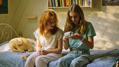 Två flickor sitter på en säng på 1980-talet.