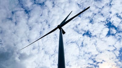 Ett vindkraftverk fotograferat underifrån mot en molnig himmel vid Tyrnselkäs vindkraftspark. 