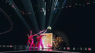 En man står på en hög träpall och håller i band som är fast i dansare nedanför. Käärijäs bidrag till Eurivisionen 2023.