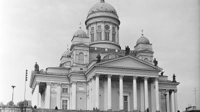 Helsingin Suurkirkko 1960-luvulla. Autoja pysäköityinä kirkon portaiden edustalle. Mies kävelee Senaatintorin poikki.