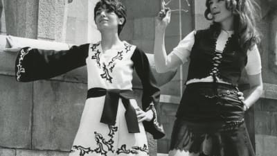 Två kvinnor klädda i minikjol poserar vid en stenvägg 1960-tal.