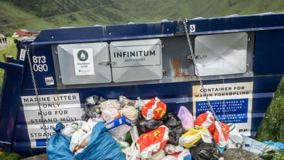 En skräpcontainer där högar av sopor ligger utanför.