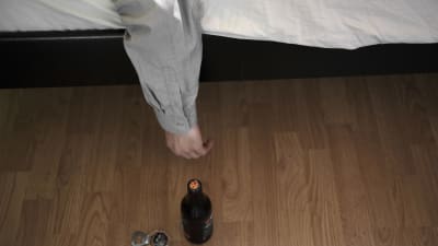 Man som ligger i sängen och sträcker sig efter en öl.