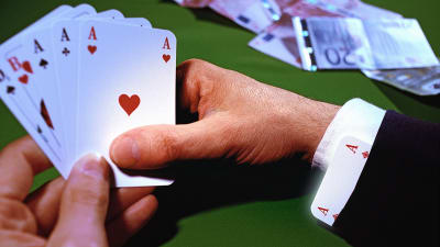 En hand håller i spelkort, på bordet ligger sedlar.