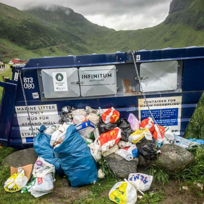 En skräpcontainer där högar av sopor ligger utanför.