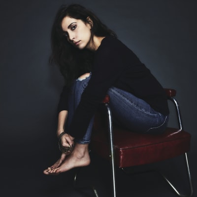 Yasmine Hamdan på en stol med repa i jeansen och barfota.