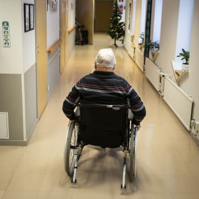 Vanha mies pyörätuolissa rullaa palvelukeskuksen käytävällä.