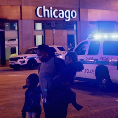 En mamma med tre barn avlägsnar sig från platsen för en masskjutning i Chicago, medan en polis dirigerar.
