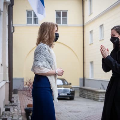 Pitkätukkainen nainen sinisessä mekossa valkoinen saali olkapäilläkohtaa mustaan takkiin pukeutuneen naisen Tallinnan vanhankaupungin sisäpihalla.