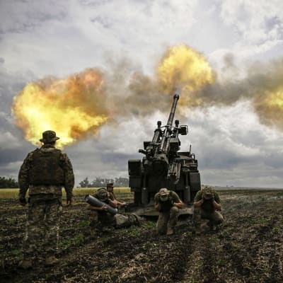 Ukrainska soldater avfyrar en haubits på en åker. Eldmoln avtecknar sig mot himlen.
