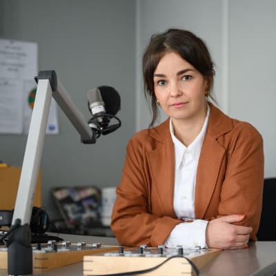 Helena Huhta sitter vid en mikrofon i en radiostudio.