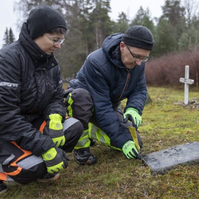 Pielaveden seurakunnan seurakuntamestari Raili Räihä ja Ylä-Savon seurakuntayhtymän seurakuntapuutarhuri Hannu Huttunen asettavat muistutus lapun hautakiven viereen.