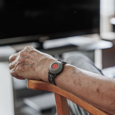 En äldre person med ett larm runt handleden, sitter framför en datorskärm.