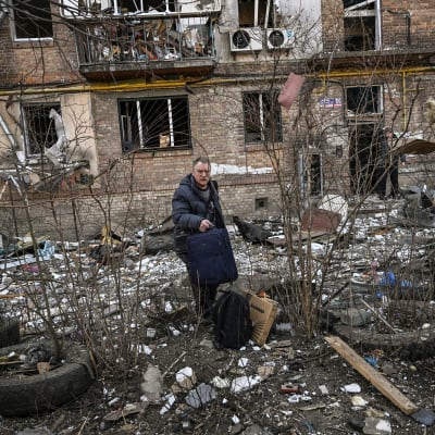 Mies seisoo tavaroineen pommituksessa tuhoutuneen asuintalon edessä.