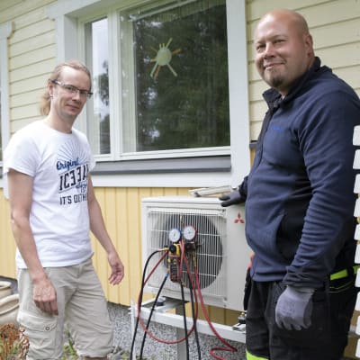 Kimmo Kostamo ja kylmälaiteasentaja Antti Varis seisovat Kostamon takapihalla ilmalämpöpumpun vieressä. 