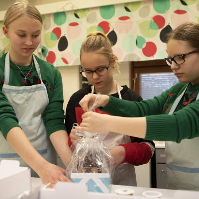 Kuopiolaisen Neulamäen koulun oppilaat Elsa Haatainen, Olivia Renkas, Saimi Tuhkanen pakkaavat piparkakkutaloa pakettiin.
