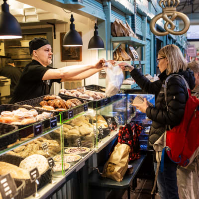 Kauppahallin Leipomon Tapani Ojala ojentaa asiakkaalle leipomo-ostokset mukaan ennen vappua huhtikuussa 2020.