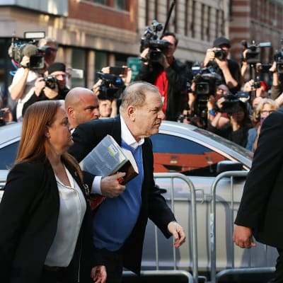 harvey Weinstein med en hög böcker under armen och pressen i bakgrunden överlämnar sig till polisen i New York.