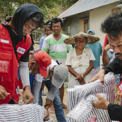 En bild på två personer som sysslar med nödhjälp i Indonesien, de håller i förnödenheter.