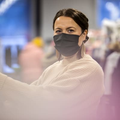Laura Ala-Kokko kirpputorilla. Hänellä on maski kasvoilla ja katsoo kameraan.