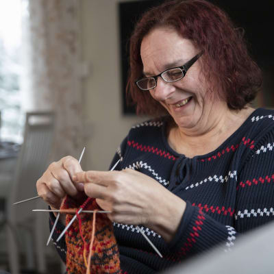 Riitta Ikonen neuloo sukkaa kotinsa sohvalla.