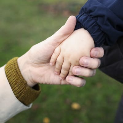 Äiti ja lapsi pitävät toisiaan kädestä lähikuvassa.