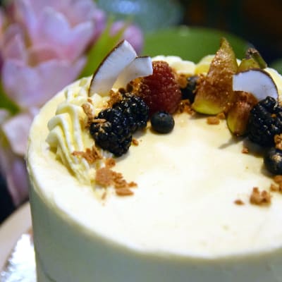 En tårta spacklad med ljus frosting och barnerad med björnbär, hallon, blåbär, fikon, kokosflarn och guldströssel.