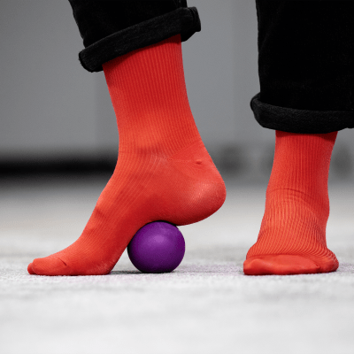Violetti faskiapallo jalkapohjan alla. Jaloissa punaiset sukat.