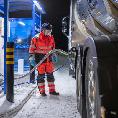 Pentti Ahopelto tankkaamassa biokaasua maitoautoonsa tammikuisena pimeänä aamuna. Hänellä on suojavisiiri ja suojahanskat kädessään.