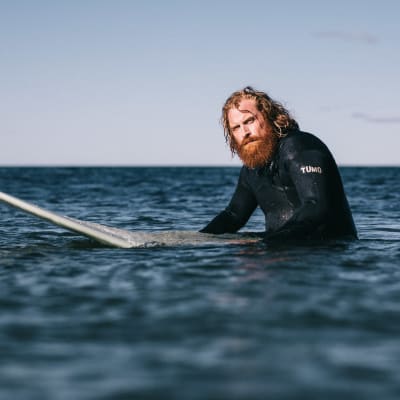 Kristofer Hivju som Erik står till midjan i vattnet med surbräda. Inga vågor.
